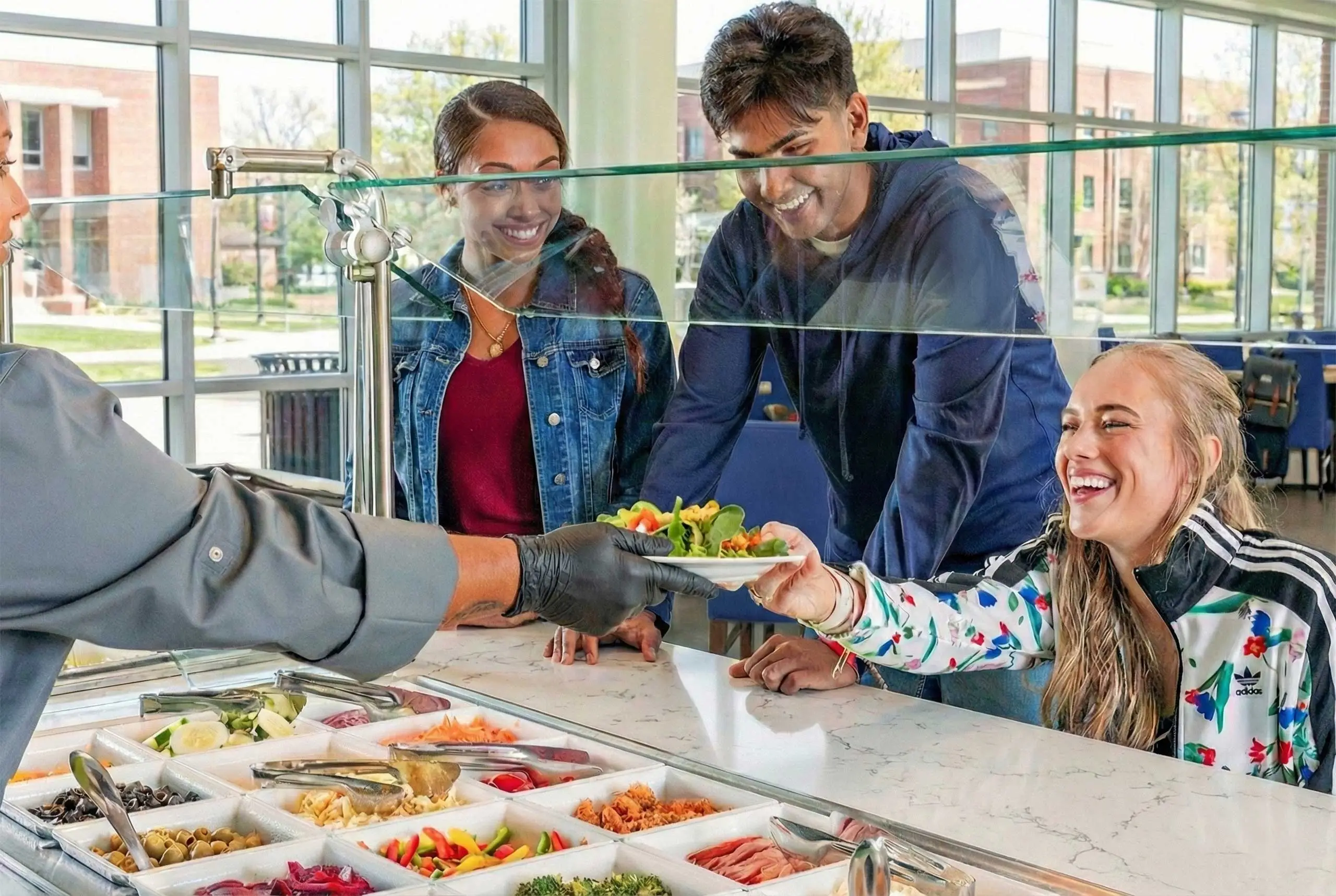 Student being served salad in dining hall while two others wait in line